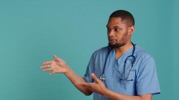 Portrait of african american nurse pointing hands towards empty space, doing advertising, talking with audience. Healthcare employee doing promotional ad, showing copy text, studio backdrop, camera A video