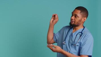 Male nurse pointing finger towards empty space doing advertising, talking with audience. Healthcare worker doing presentation, showing copy text, studio backdrop, camera A video