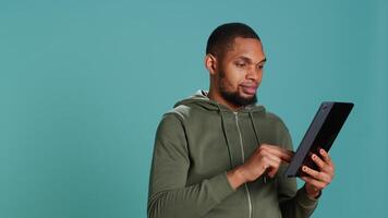 optimistisk man tillsats betalning metod på uppkopplad hemsida använder sig av läsplatta. person glada till do internet handla använder sig av enhet, skriver debitera kort data, isolerat över studio bakgrund, kamera en video