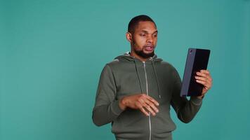 Angry man fighting with friend during videocall on tablet, isolated over studio background. Rude person in disagreement with mate, swearing and pointing finger in teleconference meeting, camera B video