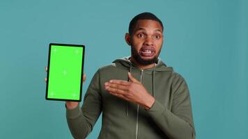 Happy influencer holding isolated screen tablet, doing recommendation, talking with audience. Cheerful person pointing towards chroma key digital device, isolated over studio background, camera A video