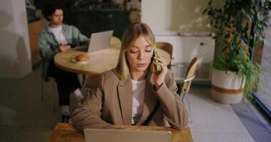 Woman Freelancer Talking By Mobile Phone And Working With Laptop In City Cafe, Portrait From Top video