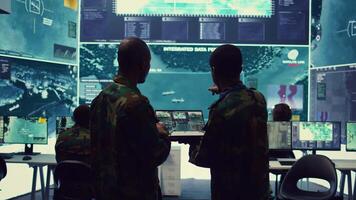 Intelligence analysts supervising and coordinating the big data analysis, processing tactical information to help the field troops. Officers monitoring real time warfare information. Camera B. video