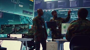 Army commanders overseeing field operations with real time data registered on surveillance CCTV systems. Military officials examining mission details, army defense program in power base. Camera B. video