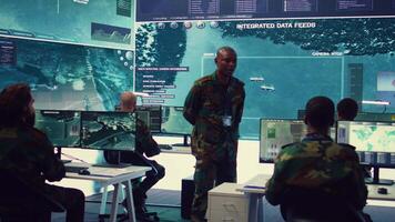 Platoon captain handling surveillance and safety operations with crew, dashboard to oversee field missions within enemy territory. Soldiers monitor CCTV satellite footage on big screen. Camera B. video