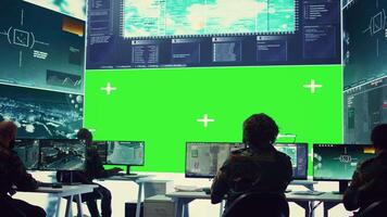 Team of IT military specialists working with a greenscreen on a big display, searching for real time data via reconnaissance CCTV system. Soldiers in power base transmitting information. Camera B. video