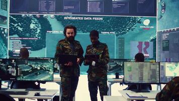 Diverse team of infantry unit leader and commander gather intelligence via radar surveillance, examine a world map to ensure national safety. Officers operating in mission control center. Camera B. video