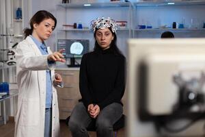 Neurologist doctor showing medicine expertise to woman patient with eeg headset during neuroscience experiment in lab, Specialist doctor analyzing brain evolution monitoring nervous system activity photo