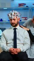 Medic in neuroscience working in neurological research laboratory developing brain experiment holding laptop explaning to man brainwave scanning headset side effects of nervous system treamtment. photo