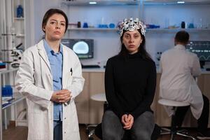 Portrait of neurologist doctor standing beside woman patient with medical eeg headset during neuroscience experiment in medical laboratory. Team of researcher analyzing brain activity evolution photo
