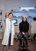 Portrait of neurologist scientist standing beside woman patient with medical eeg scanner during neuroscience experiment in clinical laboratory. Team of researcher analyzing brain activity evolution photo