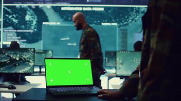 Commander examines a greenscreen on laptop in military command center, reconnaissance army division. Operator gathering intelligence from the field, transmitting real time data. Camera B. video