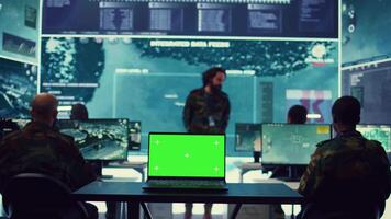 Laptop showing isolated mockup screen in army base of operations, military personnel working on gathering crucial information for a new mission. General headquarters with high tech. Camera B. video