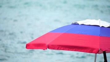 white blue red colored beach umbrellas or parasols against blue sea during a sunny day on a beach. Symbol of vacations, relax, summer. Colorful umbrellas from the sun stand on the beach. Slow motion. video