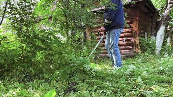 depersonalized gardener mows weeds grass. Man cutting overgrown grass in yard by using string trimmer. lawn maintenance service video