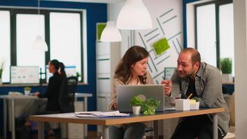 Young businesspeople using laptop, showing new startup idea, sitting at desk in modern company office. Two colleagues working together for innovative product design in creative studio. video