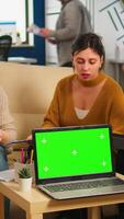 Diverse women sitting at table in start up office discussing strategy with green screen laptop in front of camera. Lady explaining to multiethnic team new project, chroma key display. mock up monitor video