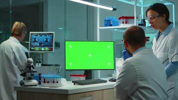 Team of microbiologists researching using computer with green screen overtime sitting in modern equipped lab. Doctors doing vaccine research writing on device with chroma key, isolated, mockup display video