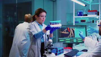 Microbiologist doctor taking a blood sample tube from rack with machines of analysis in the lab background. Doctors examining vaccine evolution using high tech researching diagnosis against covid19 video