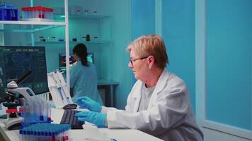 Senior biochemist writing on computer the changes in vaccine composition in modern equipped laboratory consulting with the co-worker. Examining virus evolution using high tech researching diagnosis video
