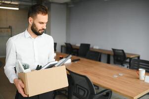 Sad Fired. Let Go Office Worker Packs His Belongings into Cardboard Box and Leaves Office. Workforce Reduction, Downsizing, Reorganization, Restructuring, Outsourcing. Mass Unemployment Market Crisis photo