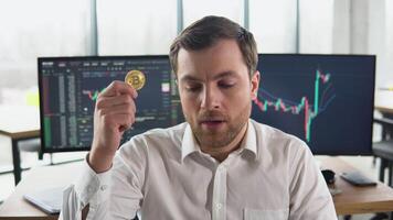 Dissapointed trader miner holding bitcoin with stock market graphs on background. Bitcoin falling. Cryptocurrency market crash. Bitcoin downtrend. Crisis of cryptocurrency video