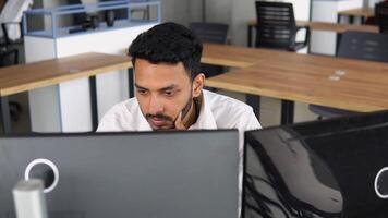 Side view of smart Indian crypto trader, investor, analyst broker, using pc analyzing digital cryptocurrency exchange, stock market charts, thinking of investing and funds risks video