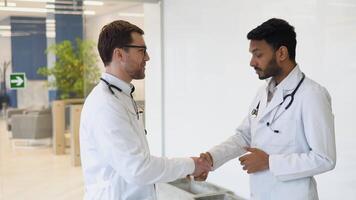 Medical multiethnic staff having discussion in a hospital hallway and handshake. Indian and caucasian smiling doctors in white coat working in a medical clinic video