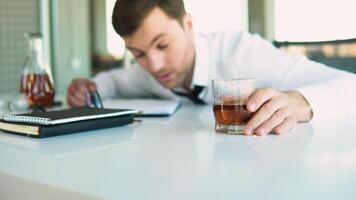 Alcoholism, drinking concept. Drunk employee sleeping at working place, holding glass with alcohol, selective focus video