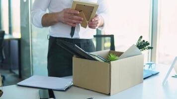 Employee putting his stuff from work desk in carton box, leaving job, close up video