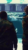 Vertical Military surveillance officers talking next to a big screen in general headquarters for cyber operations, control and monitoring to manage national security and army communications. Camera B. video