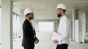 Indian and arabian builder architects in helmets handshake in a construction site. Two engineer shaking hands with deals and congratulations on success video