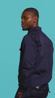 Vertical Portrait of security guard overseeing premises to prevent intrusion hearing suspect sounds, turning around. Private law enforcement worker standing isolated with back against studio backdrop, camera B video