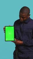 Vertical Happy security guard working protection job presenting mockup tablet. Portrait of cheerful bodyguard showcasing green screen device, isolated over studio background, camera B video