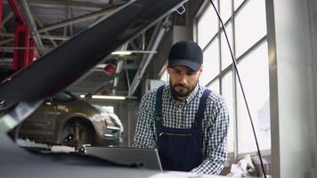 Man at the workshop in uniform using laptop for his job for fixing broken car video