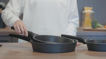 The cook collects pots. Action. A man in a white coat stands and puts one frying pan into another and collects. video