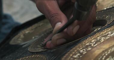 A master embosser creates a pattern on a copper plate using ancient technologies. video