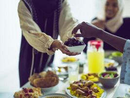 A woman in a hijab extends a platter of dates to her diverse family, creating a scene of unity and joy as they come together to break their fast during the holy month of Ramadan, symbolizing the photo