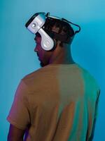 In a futuristic visual, an African American man stands isolated against a striking blue backdrop, adorned with VR glasses that transport him into a cutting-edge virtual reality experience, merging photo