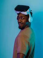 In a futuristic visual, an African American man stands isolated against a striking blue backdrop, adorned with VR glasses that transport him into a cutting-edge virtual reality experience, merging photo