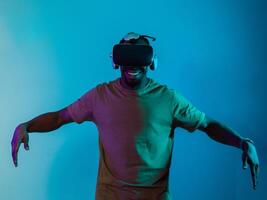 African American man dons VR glasses, engrossed in a virtual reality simulation, gesturing with hands, against a striking blue background, highlighting the fusion of cutting-edge technology and photo