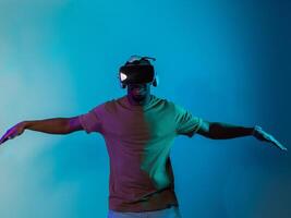 African American man dons VR glasses, engrossed in a virtual reality simulation, gesturing with hands, against a striking blue background, highlighting the fusion of cutting-edge technology and photo