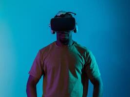 In a futuristic visual, an African American man stands isolated against a striking blue backdrop, adorned with VR glasses that transport him into a cutting-edge virtual reality experience, merging photo