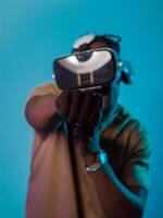 In an avant-garde scene, an African American man engages in cutting-edge virtual reality gaming, utilizing VR glasses to immerse himself in futuristic boxing games, set against a vivid blue background photo