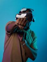 In an avant-garde scene, an African American man engages in cutting-edge virtual reality gaming, utilizing VR glasses to immerse himself in futuristic boxing games, set against a vivid blue background photo