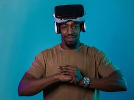 In an avant-garde scene, an African American man engages in cutting-edge virtual reality gaming, utilizing VR glasses to immerse himself in futuristic boxing games, set against a vivid blue background photo