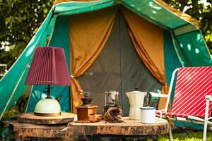 selective focus of vintage coffee set on the old wooden table In front of the retro cabin tent, Antique oil lamp, retro chairs, Group of camping tents, and soft focus. photo