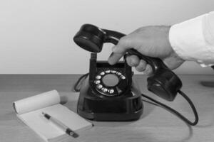 Old telephone set on a wooden table, Man's hand dialing a phone number on a phone disk. retro installation. Black and white photo