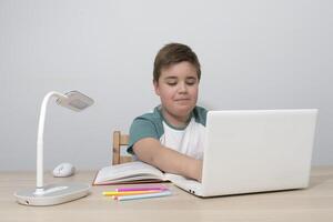 Boy teenager with a computer at the table. Typing on the keyboard with positive emotion photo