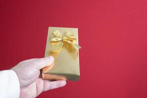 A beautiful gift in a golden package in a man's hand with a bow. on a red background close-up. place for text photo